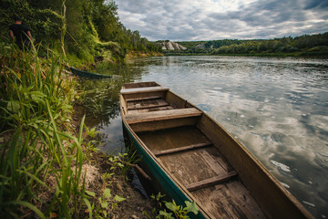 abandoned old wooden fishing boat near pier in summer lake or river. beautiful summer sunny day or evening.