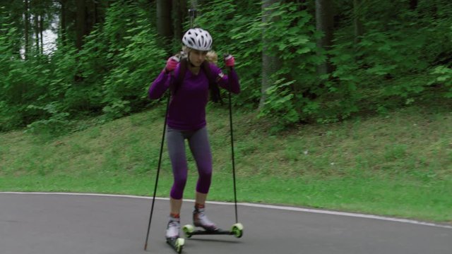 TRACKING Caucasian female professional biathlete roller skiing uphill on a forest track during mid-season practice in summer. ARRI Alexa Mini with Cooke S4 prime lenses RAW graded footage