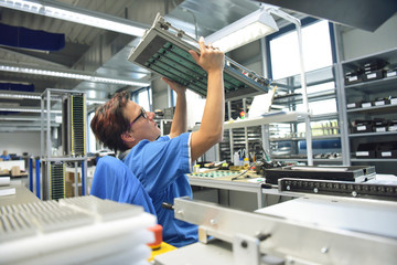 Arbeiterin in modernen Werk kontrolliert elektronisches Bauteil in der Fertigung // quality control - woman checking motherboard - working in the production of a factory for electronics
