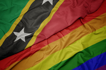 waving colorful gay rainbow flag and national flag of saint kitts and nevis.