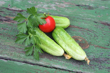Organic green cucumbers and tomato on the background of boards