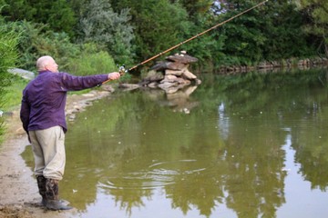 Peaceful Scene of Middle Aged Man Fishing on a Country Pond at Sunset with Golden filtered light reflected on pond