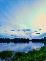 landscape photo of a lake with grass and forest in the background with a beautiful sky with cirrus clouds in the evening using a polarizing filter