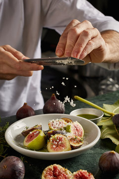 Chefs hands grating Parmesan on halved figs