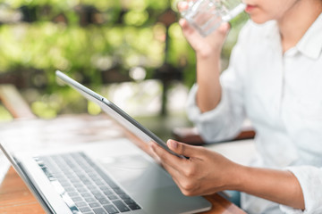 A girl works at laptop in a cafe, woman's fingers typing on the keyboard. Workplace in a cafe, a cup of coffee next to a laptop, toned bright sunny photo
