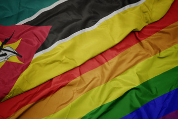 waving colorful gay rainbow flag and national flag of mozambique.