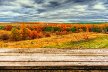 Naklejka na ściany i meble Empty wooden table with blurred picturesque autumn landscape of panoramic view from hill to lowland with field and grove in cloudy day. Mock up for display or montage products