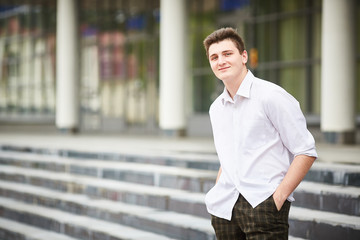 Young handsome smiling businessman is standing on steps near a business building