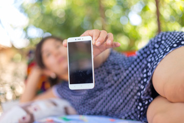 a young woman lies on a bed and photographs herself on the phone. Cheerful attractive woman in a blue pea shirt posing for a selfie. Social media concept