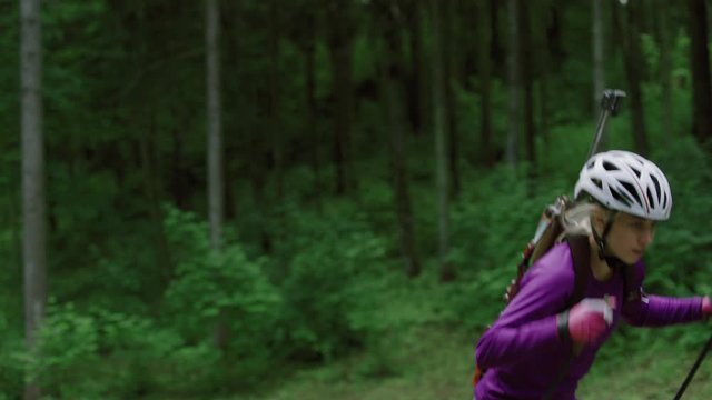 TRACKING Caucasian female professional biathlete roller skiing uphill on a forest track during mid-season practice in summer. ARRI Alexa Mini with Cooke S4 prime lenses RAW graded footage