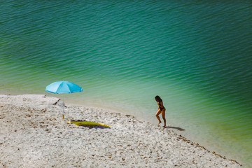 Fototapeta na wymiar woman in swimsuit walking by sand beach blue sun umbrella and yellow blanket