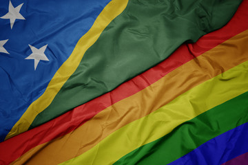 waving colorful gay rainbow flag and national flag of Solomon Islands.