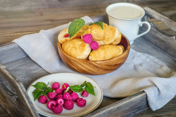 Croissants with raspberries on a wooden tray. The concept of a wholesome breakfast.