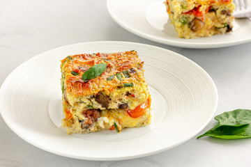 Slice of Breakfast Egg Casserole on a White Plate Close Up Photo.