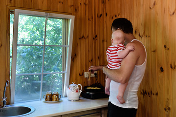Father with a small baby in his arms is cooking dinner. Interior of a country house