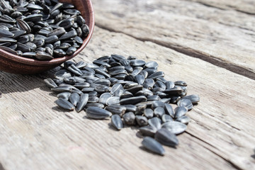 A pile of sunflower seeds in a bowl on a wooden background. Sunflower seeds scattered on the table.