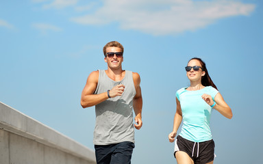 fitness, sport and lifestyle concept - happy couple in sports clothes and sunglasses running...