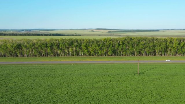 Road in Russia.Sedan cars driving fast on the road and overtaking slower driving cars.Highway between fields. Fields on the hills in the far background.