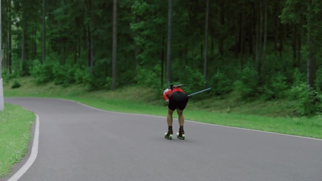 TRACKING Caucasian male professional biathlete roller skiing downhill on a forest track during mid-season practice in summer. ARRI Alexa Mini with Cooke S4 prime lenses RAW graded footage