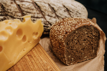 Fresh bread and cheese on paper on wooden black background