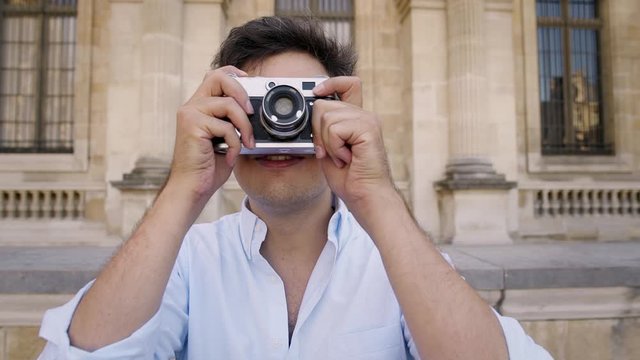 PARIS, FRANCE, APRIL 2019. Gimbal slow motion portrait shot of smiling young man in white shirt and eyeglasses with a film camera making looking at the sky laughing on background of Louvre museum