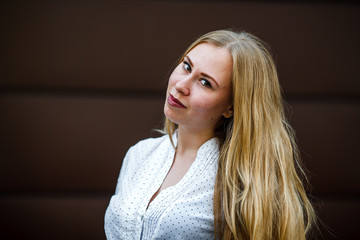 Portrait of a young cute caucasian girl with problem skin in white shirt opposite brown background on the street in spring.