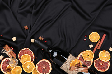 Dried citrus fruits with cinnamon, star anise and bottle of wine on black satin fabric background
