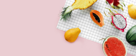 Flat lay tropical summer fruit on a white grid and pastel pink background, creative summer food...