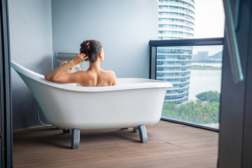 Woman relaxing in outdoor bath on a balcony with sea view