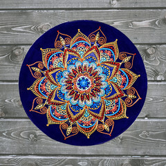 Decorative ceramic plate, hand painted with acrylic paints on a wooden background. A square photo closeup.