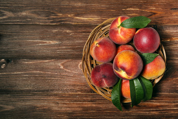 Fresh peaches with green leafs in basket on brown wooden table