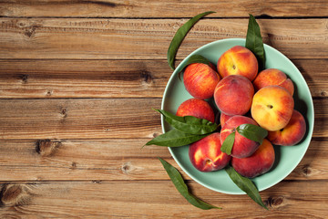 Fresh peaches with green leafs in plate on brown wooden table