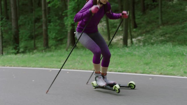 TRACKING Caucasian female professional biathlete roller skiing uphill on a forest track during mid-season practice in summer. ARRI Alexa Mini with Cooke S4 prime lenses RAW graded footage