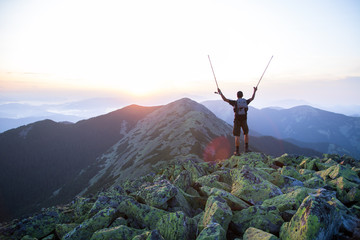 caucasian man hiker is on the peak of green stones mountain watching sunset with trekking sticks in...