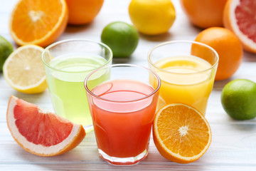 Citrus juice in glasses with fruits on white wooden table