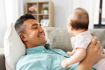 family, parenthood and fatherhood concept - happy smiling middle aged father with little baby daughter lying on sofa at home