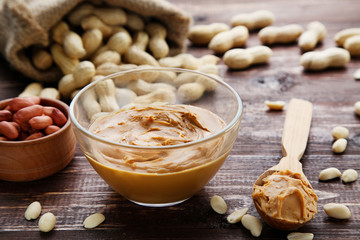 Peanut butter in bowl and nuts on brown wooden table