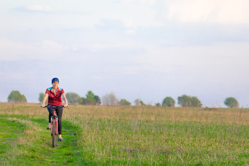 Naklejka na ściany i meble Girl on a bicycle on a background of blue sky and green grass