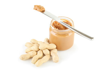 Peanut butter in glass jar with nuts and knife isolated on white background