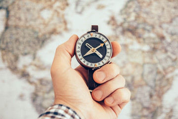 Close up of man hand holding vintage compass with world map as background. Travel and Business planning concept