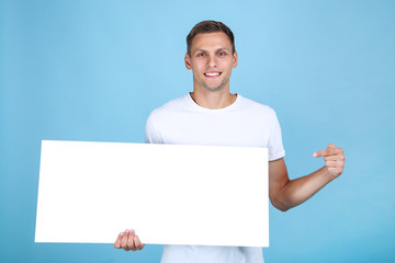 Young man with blank board on blue background