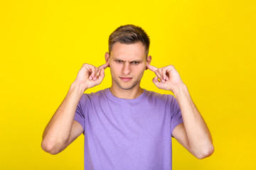 Young man closed ears by hands on yellow background