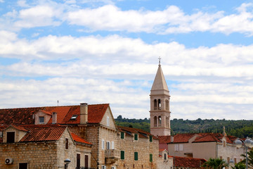 Fototapeta premium Traditional stone architecture and landmark Church of Mary's Annunciation bell tower in small town Supetar, on island Brac, Croatia.