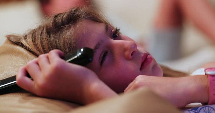 Little girl watching TV screen in couch at home in the evning. Child in front of TV