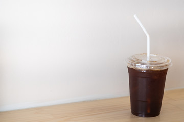 Close up of take away plastic cup of iced black coffee Americano on wooden table in restaurant.