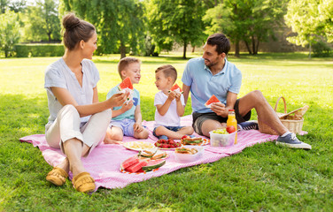 family, leisure and people concept - happy mother, father and two little sons having picnic and eating watermelon at summer park