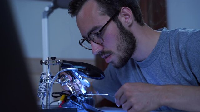 Portrait of skill young bearded man in glasses working with a soldering iron at his working place. Concept of the profession, accurate work, engineer position