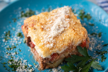 greek moussaka on blue plate in white wooden background