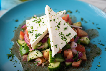 greek salad with chunk feta cheese on blue plate