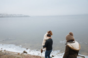 family in coats walking and having fun on the banks of a frozen river. back view